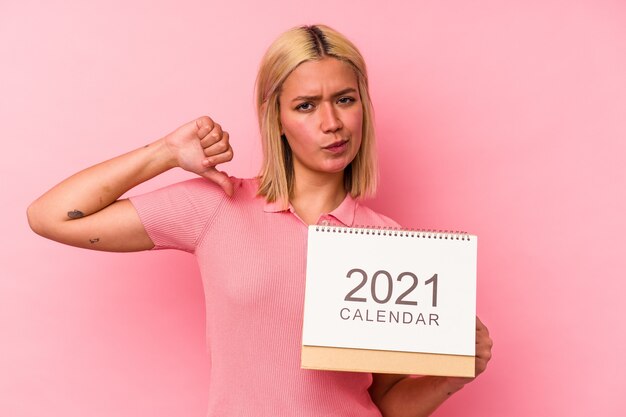 Joven venezolana sosteniendo un calendario 2021 aislado en una pared rosa se siente orgullosa y segura de sí misma, ejemplo a seguir.