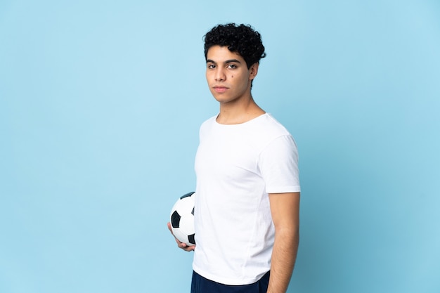 Joven venezolano aislado en azul con balón de fútbol