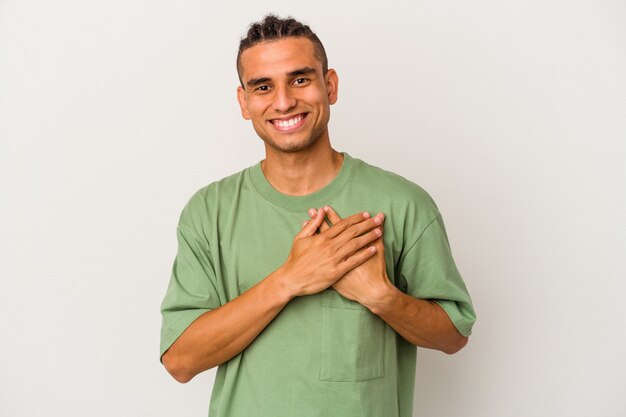 Joven venezolano aislado sobre fondo blanco riendo manteniendo las manos en el corazón, concepto de felicidad.