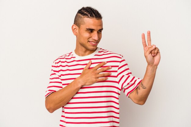 Joven venezolano aislado sobre fondo blanco tomando un juramento, poniendo la mano en el pecho.