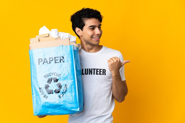 Joven venezolano sosteniendo una bolsa de reciclaje llena de papel para reciclar apuntando hacia el lado para presentar un producto