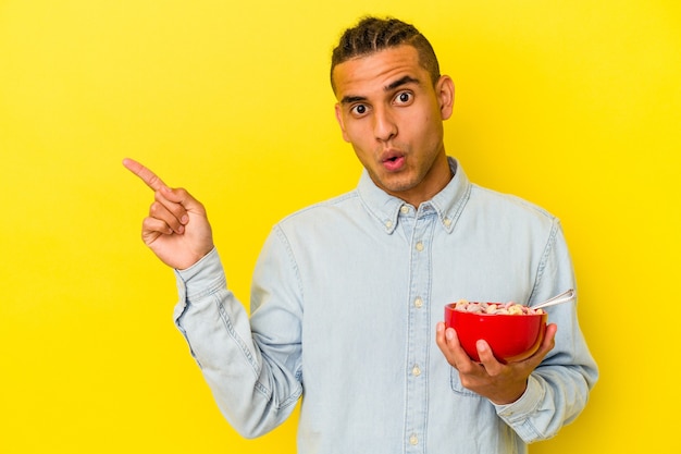 Joven venezolano sosteniendo un tazón de cereales aislado en la pared amarilla apuntando hacia el lado