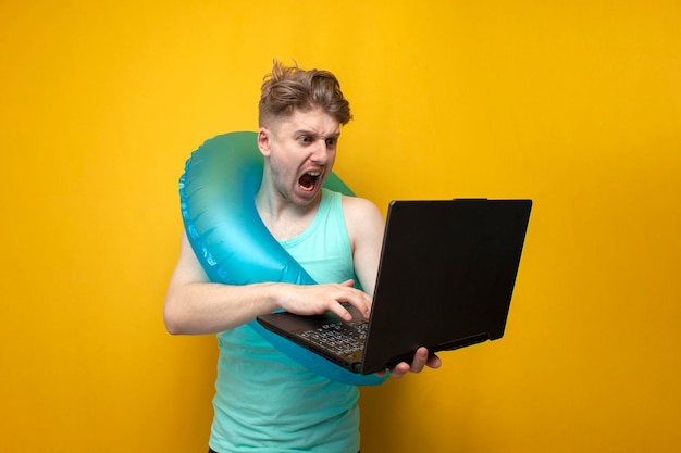 Un joven en verano de vacaciones con un anillo de natación inflable sosteniendo una computadora portátil y gritando