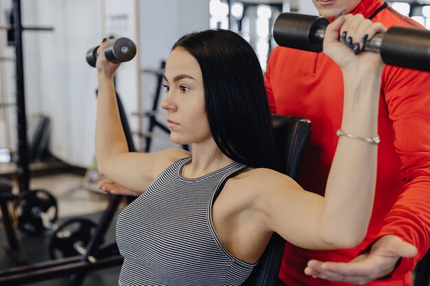 Una joven vestida con ropa deportiva en un gimnasio realiza ejercicios con mancuernas