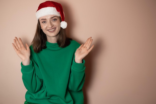 una joven vestida con un suéter verde en la cabeza un sombrero de santa extiende los brazos con sorpresa