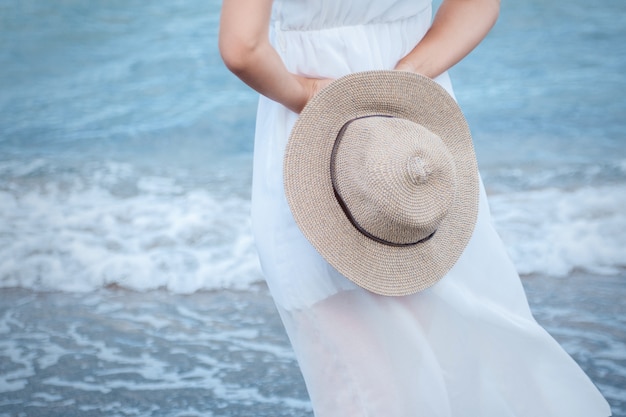 Una joven con un vestido blanco se encuentra de espaldas en la orilla del mar azul