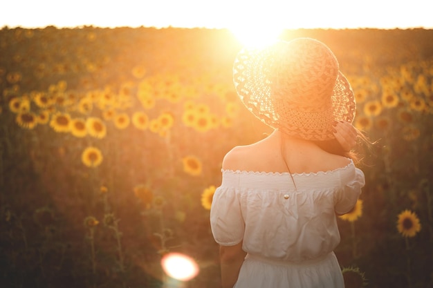 Una joven con un vestido blanco y un sombrero en un campo de girasoles al atardecer Retrato de una mujer con una figura delgada sobre un fondo de flores amarillas