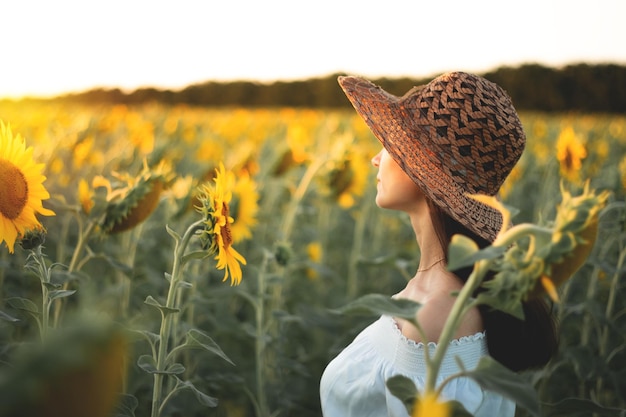 Una joven con un vestido blanco y un sombrero en un campo de girasoles al atardecer Retrato de una mujer con una figura delgada sobre un fondo de flores amarillas