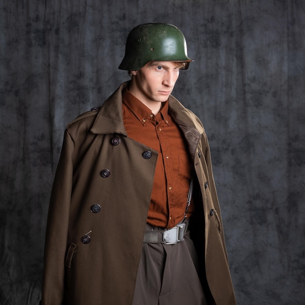 Un joven vestido de estilo militar con un traje marrón y un casco en la cabeza posando en el estudio en