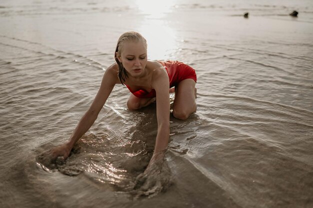 Una joven con un vestido rojo yace en el agua del mar.