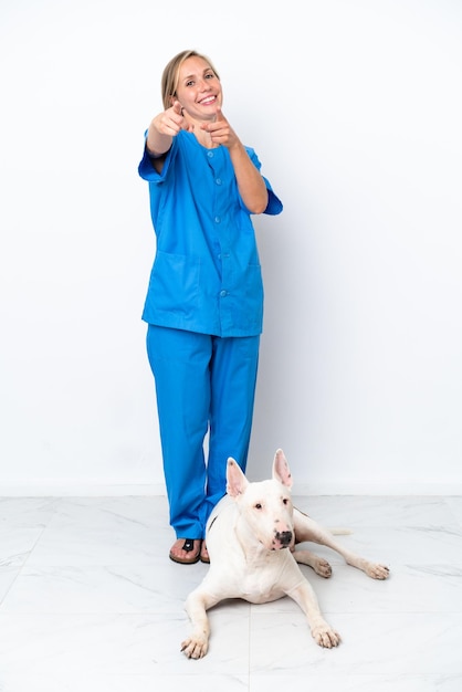 Una joven veterinaria inglesa con un perro aislado de fondo blanco te señala con una expresión de confianza