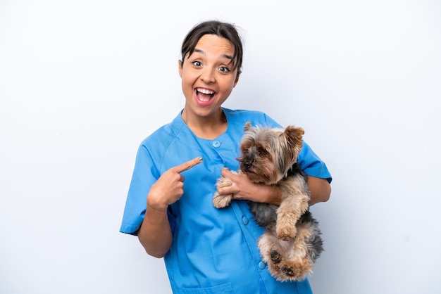 Joven veterinaria con perro aislado de fondo blanco sorprendida y señalando con el dedo al costado