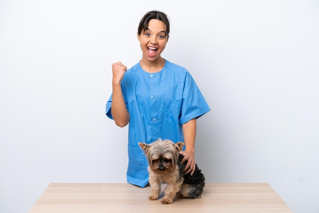 Joven veterinaria con perro en una mesa aislada de fondo blanco celebrando una victoria