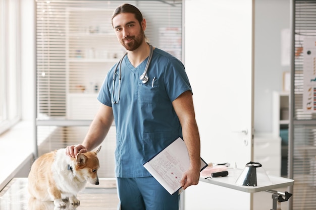 Joven veterinario confiado en uniforme azul de pie junto al lugar de trabajo