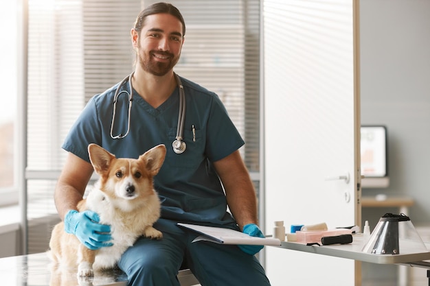 Joven veterinario exitoso en uniforme sentado en el lugar de trabajo en clínicas