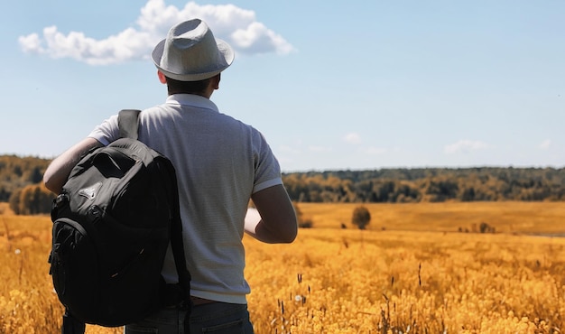 Un joven viaja en la naturaleza. Viajando con una mochila a los hombros por un hermoso parque. Hacer autostop con una bolsa en otoño.