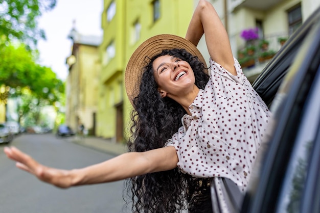 Joven viajando en coche mujer hispana con pelo rizado mirando por la ventana disfrutando de vacaciones