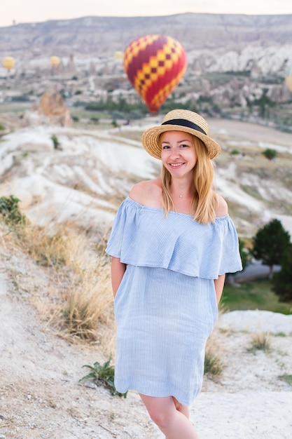 Joven viajera feliz con vestido azul y sombrero de paja disfrutando de los globos aerostáticos de Capadocia Turquía