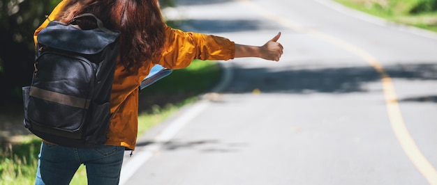 Una joven viajera haciendo autostop y deteniendo el coche con los pulgares hacia arriba en una carretera de montaña