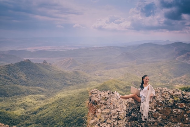 Joven viajera independiente que trabaja en línea en cualquier lugar al aire libre usando una computadora portátil disfrutando del pico de la montaña