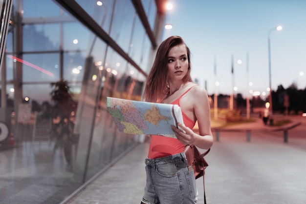 Joven viajera sosteniendo el mapa y buscando el lugar al atardecer