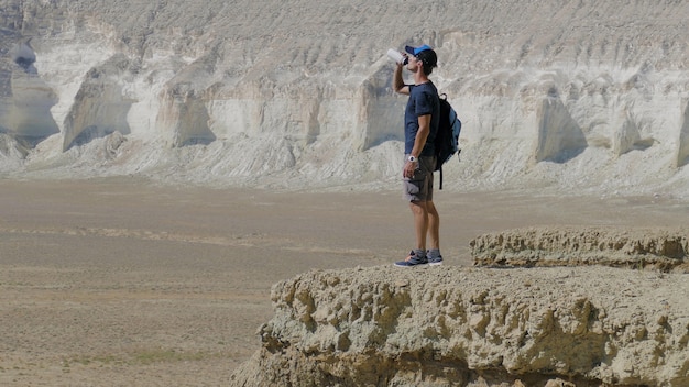 Un joven viajero bebe agua contra las rocas.