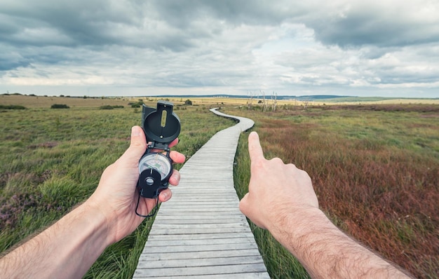 Joven viajero buscando dirección con una brújula en el paisaje con paseo marítimo de madera. Toma de punto de vista