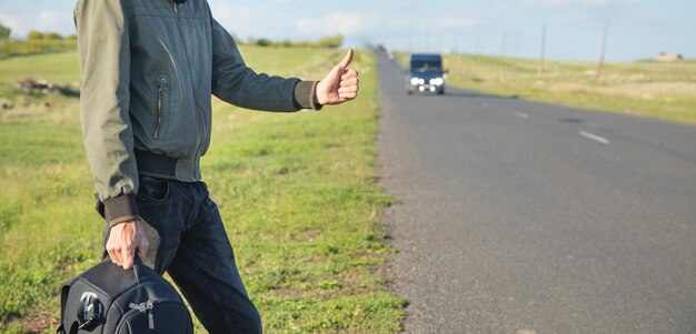 Joven viajero haciendo autostop intenta atrapar un auto en una carretera