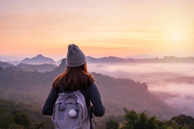 Joven viajero mirando al mar de niebla y puesta de sol sobre la montaña