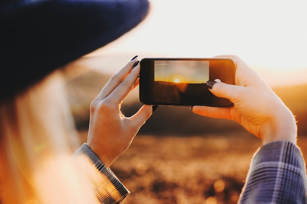 Joven viajero mujer rubia tomando una foto de una puesta de sol épica mientras viaja en su tiempo de vacaciones de primavera.