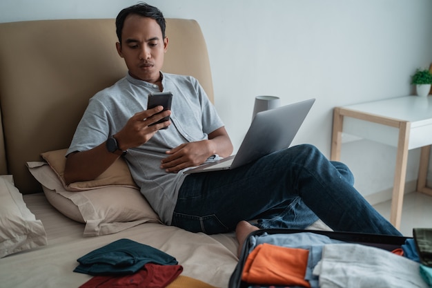 Joven viajero usando laptop con maleta llena de ropa