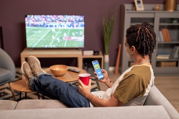 Foto joven viendo un partido de fútbol en casa y relajándose en el sofá