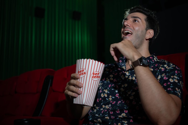 Joven viendo una película y comiendo palomitas de maíz mientras está sentado en el sofá rojo