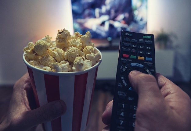 Joven viendo una película en su sala de estar con palomitas de maíz y control remoto Toma de punto de vista