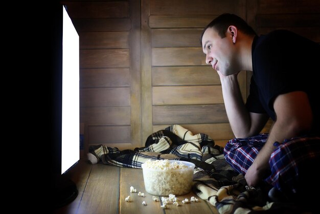 Joven viendo la televisión en casa en el suelo y comiendo palomitas de maíz