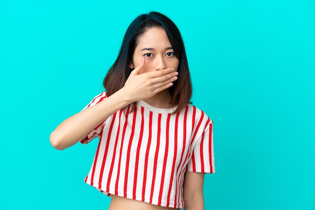 Joven vietnamita aislada de fondo azul cubriendo la boca con la mano