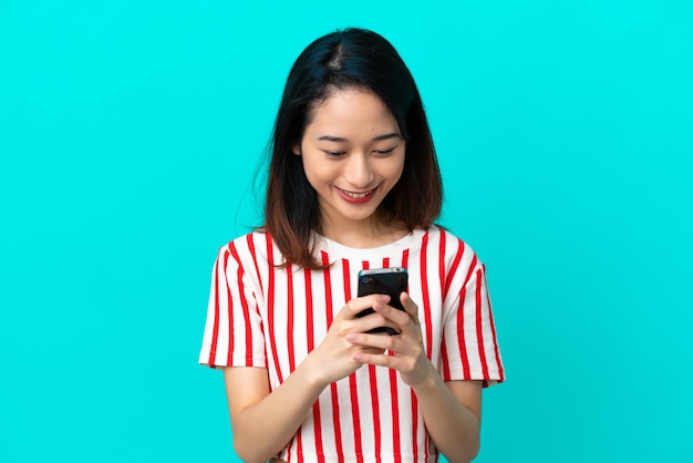 Joven vietnamita aislada de fondo azul enviando un mensaje con el móvil