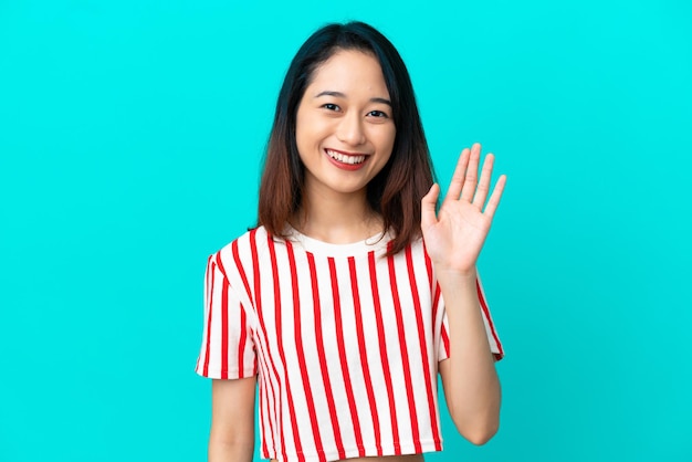 Joven vietnamita aislada de fondo azul saludando con la mano con expresión feliz