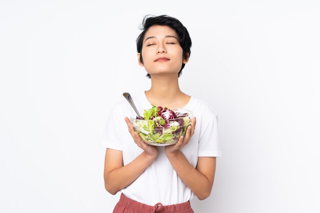 Joven vietnamita con el pelo corto con una ensalada sobre pared aislada