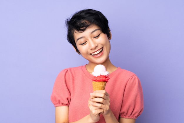 Joven vietnamita con el pelo corto con un helado de cucurucho sobre pared púrpura