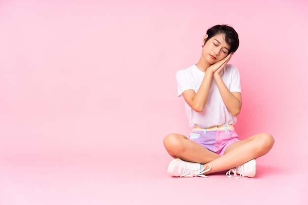 Joven vietnamita con el pelo corto sentada en el suelo sobre rosa aislado