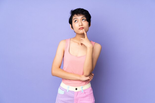 Joven vietnamita con el pelo corto sobre la pared púrpura que tiene dudas mientras mira hacia arriba