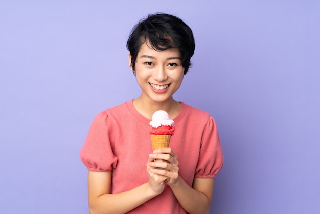 Joven vietnamita con el pelo corto sosteniendo un helado de cucurucho sobre pared púrpura aislado