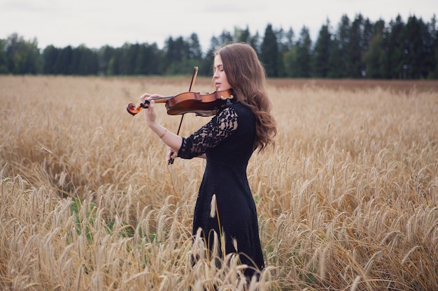 Una joven violinista toca magistralmente su instrumento de pie sobre un campo de trigo maduro