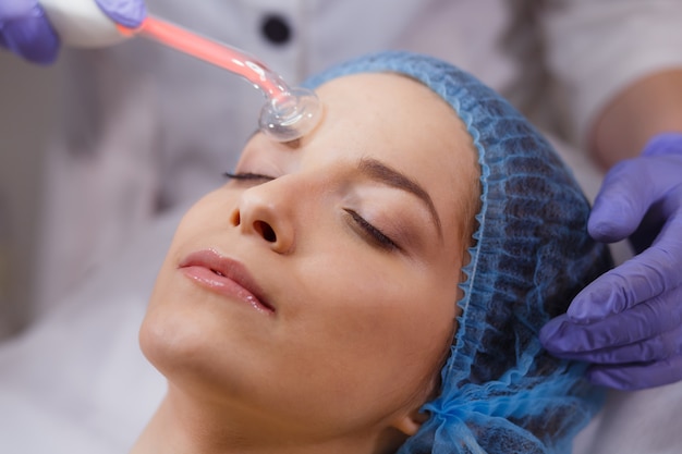 Una joven visitó a un dermatólogo. Recepción de un masaje eléctrico con masaje facial en el salón de belleza.