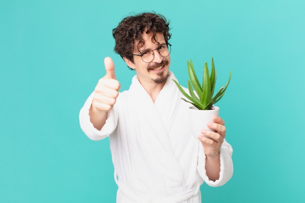 Joven vistiendo albornoz sintiéndose orgulloso, sonriendo positivamente con los pulgares hacia arriba