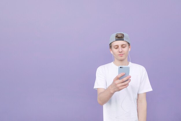 Joven vistiendo una camiseta blanca y gorra está escuchando música en los auriculares