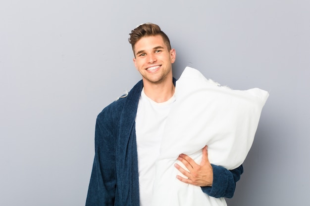 Joven vistiendo pijama sosteniendo una almohada feliz, sonriente y alegre.