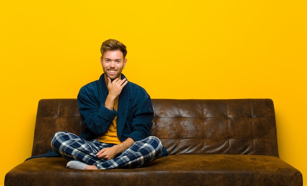 Joven vistiendo pijamas sonriendo, disfrutando de la vida, sintiéndose feliz, amigable, satisfecho y despreocupado con la mano