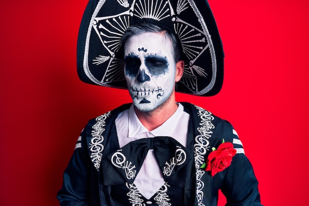 Joven vistiendo traje mexicano del día de los muertos sobre rojo con la mano en el estómago porque indigestión enfermedad dolorosa sensación de malestar dolor concepto